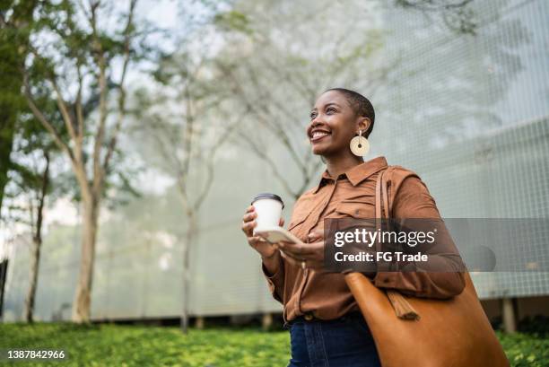 mujer de negocios sosteniendo un teléfono inteligente y mirando hacia otro lado al aire libre - woman outdoors fotografías e imágenes de stock