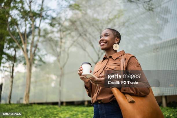 business woman holding smartphone and looking away outdoors - businesswear stock pictures, royalty-free photos & images