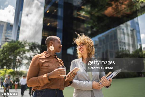business women talking while walking outdoors - two women talking stockfoto's en -beelden