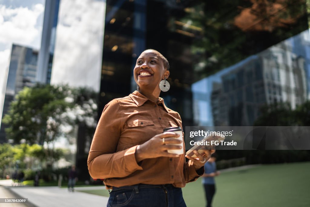 Mujer de negocios sosteniendo un teléfono inteligente y mirando hacia otro lado al aire libre