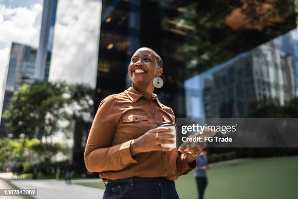 mujer de negocios sosteniendo un teléfono inteligente y mirando hacia otro lado al aire libre - mujer feliz fotografías e imágenes de stock