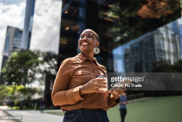 business woman holding smartphone and looking away outdoors - levensstijl stockfoto's en -beelden