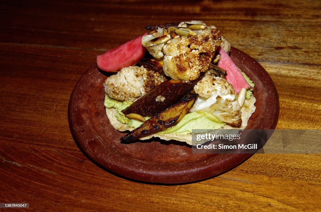 Vegan tostada topped with pureed avocado, roasted cauliflower, heirloom carrots and pickled radish and garnished with pumpkin seeds