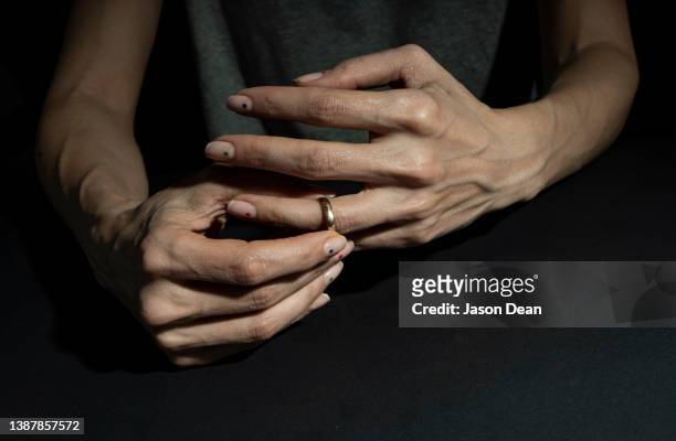 a woman divorcing and taking off her wedding ring in a moody background - divorcio fotografías e imágenes de stock