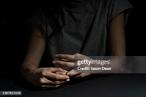 A woman divorcing and taking off her wedding ring in a moody background A woman divorcing and taking off her wedding ring in a moody background