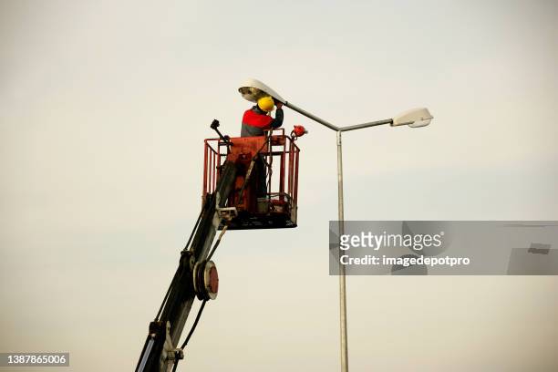 técnico trabaja en un cubo en lo alto de un poste de alumbrado público - street light fotografías e imágenes de stock