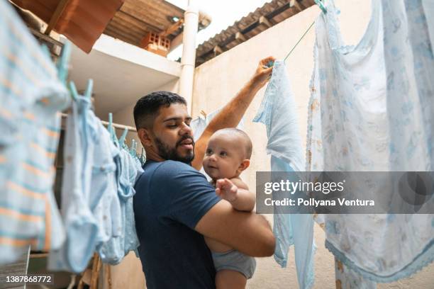 padre colgando ropa en tendedero mientras cuida al bebé - tarea doméstica fotografías e imágenes de stock