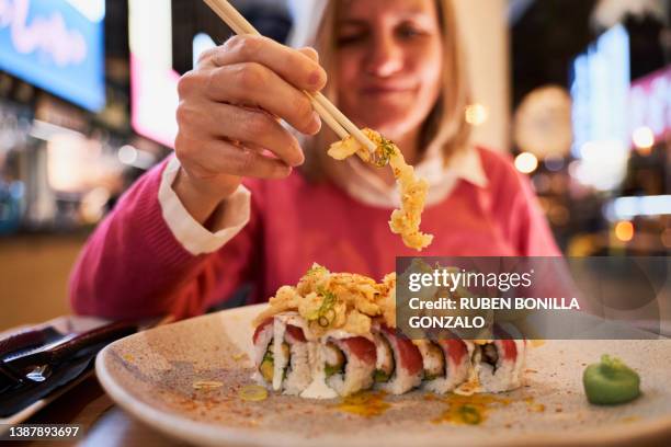 caucasian woman taking a sushi piece on chopsticks from a plate in a japanese restaurant. food concept - sushi restaurant 個照片及圖片檔