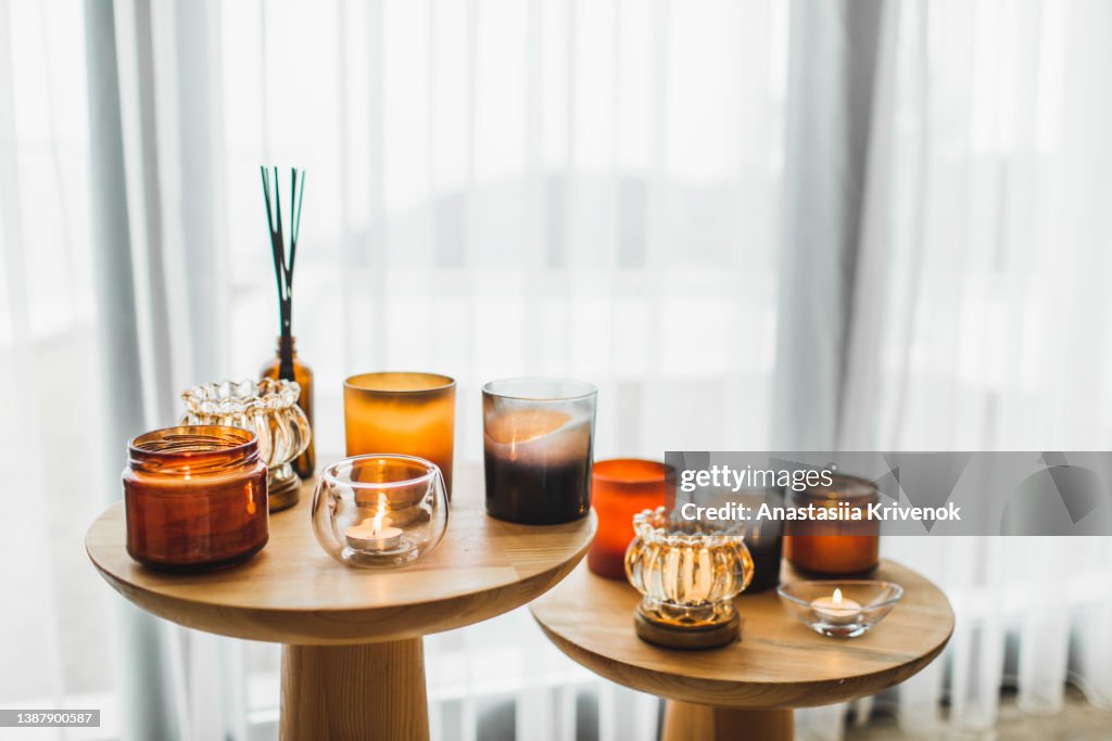 Scented candles in different candlelights on wooden table at home.