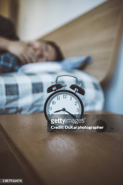 man in bed reaching for alarm clock. - alarm clock hand stock pictures, royalty-free photos & images