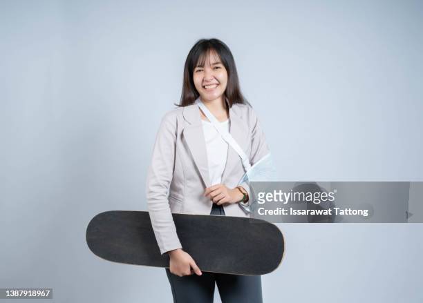 woman smile broken arm after accident wear arm splint for treatment she play skateboard skating accident sport extreme, happy asian female sling support hand isolated on gray background - broken skateboard stockfoto's en -beelden