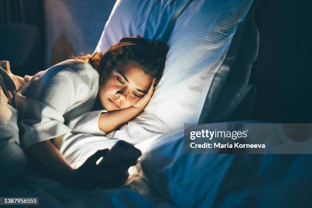 young woman laying in bed and using smart phone. - générique photos et images de collection