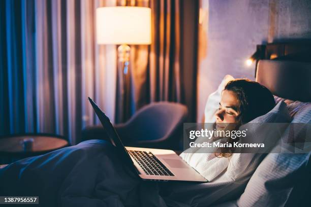 young woman laying in bed and using laptop at the night. - hotel room work stock-fotos und bilder