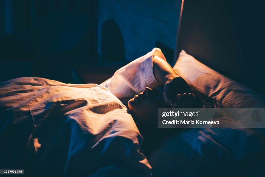 Woman with Insomnia. Young woman lying on bed with hand on forehead.
