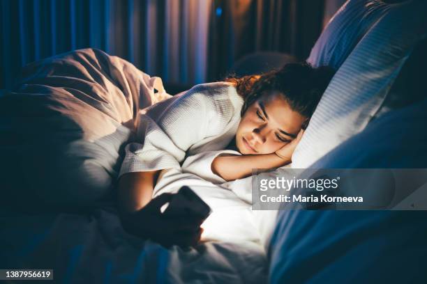 young woman laying in bed and using smart phone. - can't sleep stock-fotos und bilder