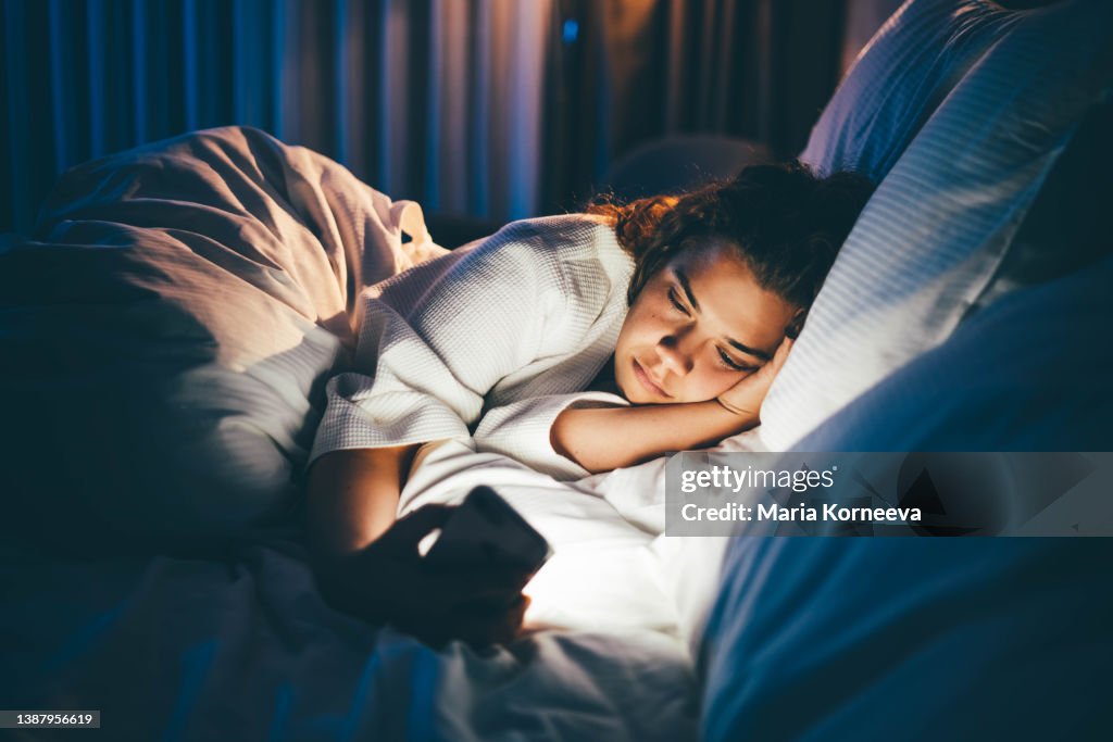 Young woman laying in bed and using smart phone.