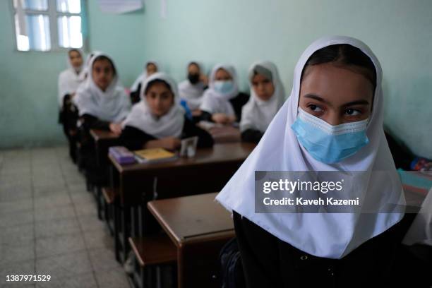 Sixth grade girl in school uniform and covered in veil weariing a COVID-19 protective facial mask sits in a classroom in Tajrobawai girls primary and...