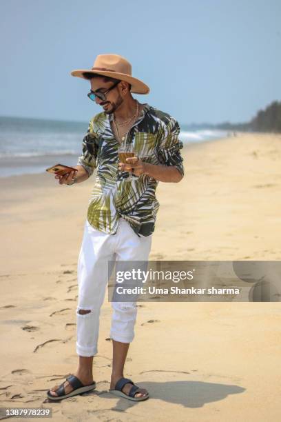 man walking on beach holding champagne glass and using phone. - kerala beach stockfoto's en -beelden