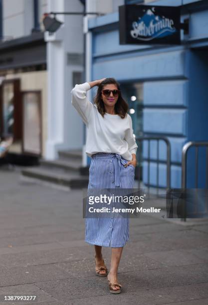 Anna Wolfers wearing brown shades, a white sweater, a blue and white striped midi dress and beige sandals via goldigshop.de on March 25, 2022 in...