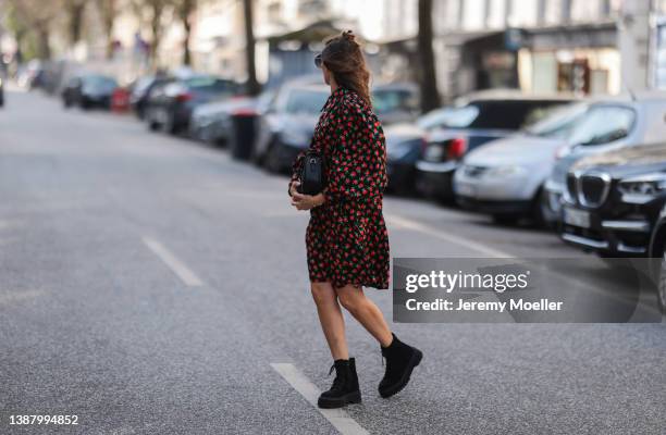 Anna Wolfers wearing black shades, a red and black floral mini dress, a black leather bag and black boots via goldigshop.de on March 25, 2022 in...