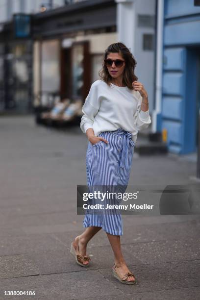 Anna Wolfers wearing brown shades, a white sweater, a blue and white striped midi dress and beige sandals via goldigshop.de on March 25, 2022 in...