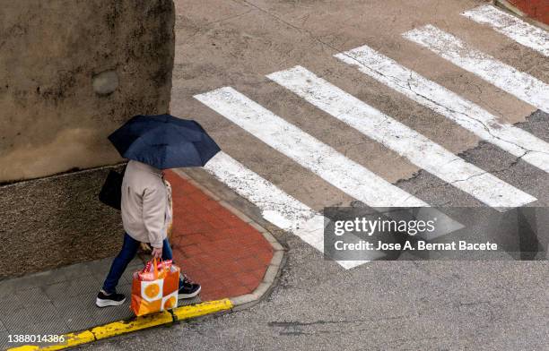 high angle view, woman walking with umbrella and shopping bag on a rainy day in the city. - torrential rain umbrella stock pictures, royalty-free photos & images