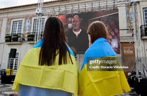 Two girls wrapped in Ukrainian flags watch British singer Sting on a giant screen at City Hall as part of the international charity TV marathon in...