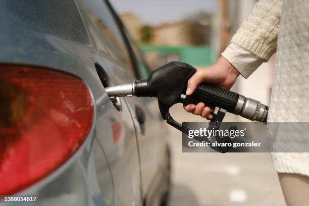 unrecognizable woman using gas pump to add fuel to her car during energy crisis - fare benzina foto e immagini stock