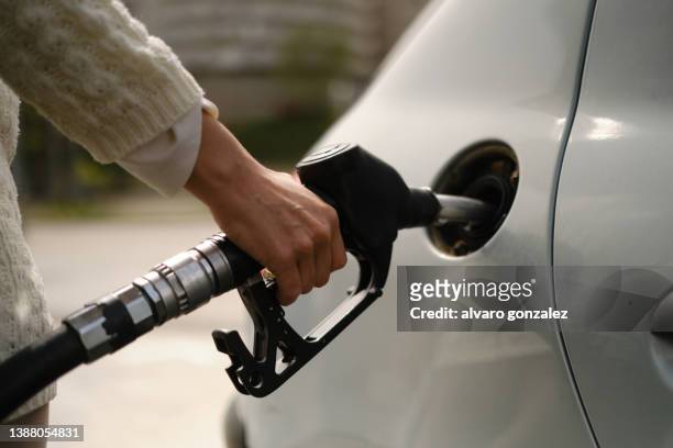 a woman using a gas pump to refuel vehicle during energy crisis - fare il pieno di benzina foto e immagini stock