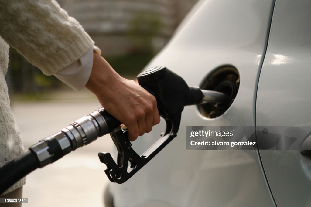A woman using a gas pump to refuel vehicle during energy crisis
