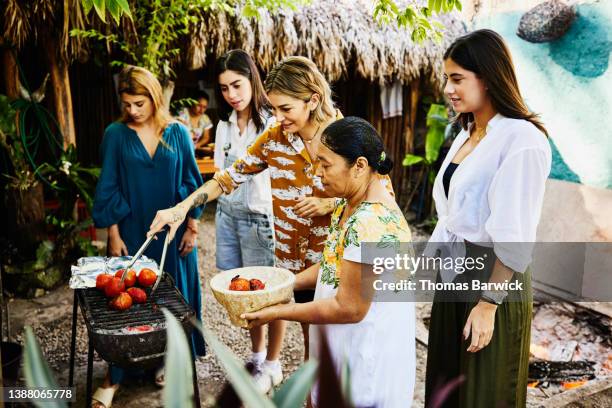 medium wide shot of smiling woman taking tomatoes off grill during traditional mayan cooking class - local economy of mexico stock pictures, royalty-free photos & images