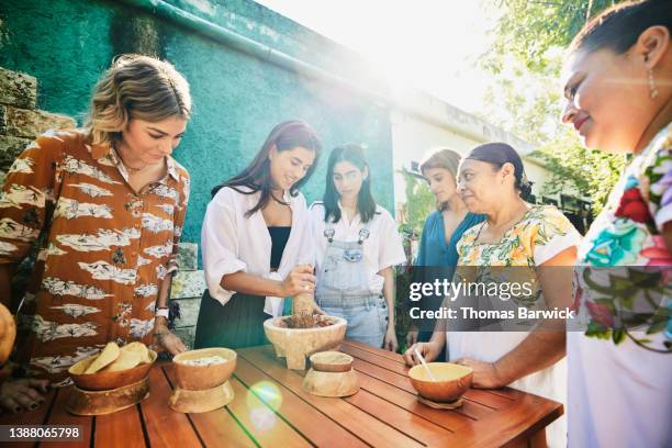 medium wide shot of smiling friends grinding salsa in mortar during traditional mayan cooking class - eco tourism stock pictures, royalty-free photos & images