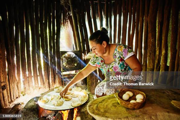 Medium wide shot of woman cooking egg filled tortillas over fire while teaching Mayan cooking class