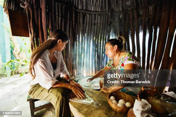 Medium wide shot of woman learning to make egg filled tortillas over fire during traditional Mayan cooking class