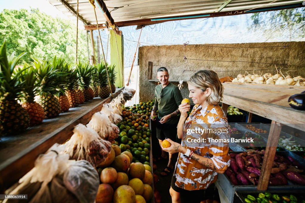 Wide shot of smiling woman smelling fruit while shopping at local market during vacation