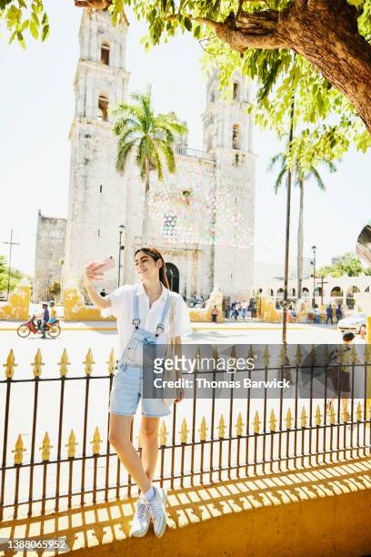 Wide shot of smiling woman taking selfie while exploring historic town while on vacation