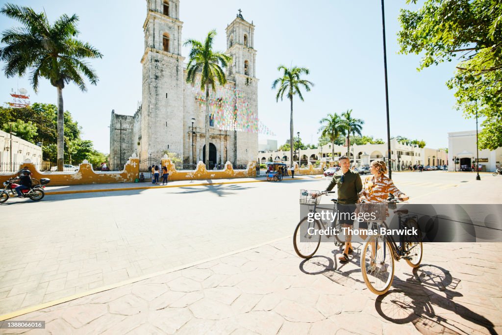 Wide shot of couple walking bikes through historic town while on vacation