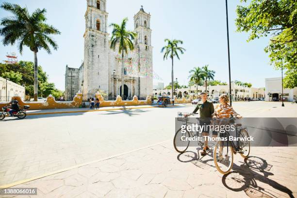 Wide shot of couple walking bikes through historic town while on vacation