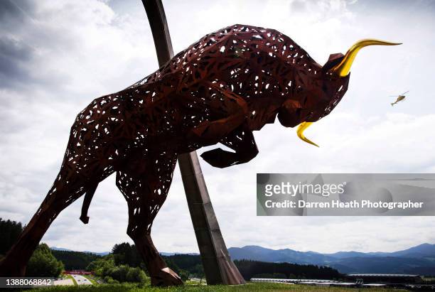 The very large scale rusty metal Red Bull Bull sculpture and arch that stands atop a hill overlooking the Red Bull Ring Circuit while Formula One...