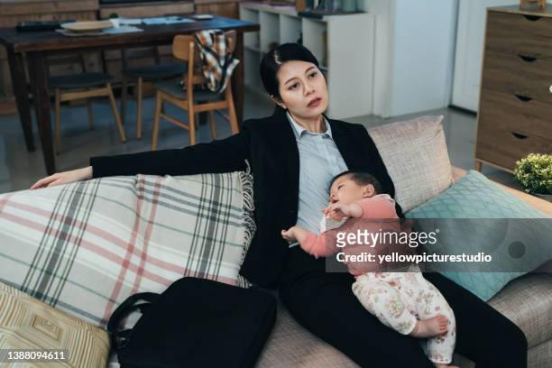 porträt überwältigte koreanische berufstätige mutter, die mit ihrem schlafenden kleinen kind auf der couch sitzt. asiatische karrierefrau fühlt sich erschöpft, nachdem sie das kind eingeschläfert hat. pseudo-alleinerziehende und lifestyle-konzept - stressed young woman sitting on couch stock-fotos und bilder