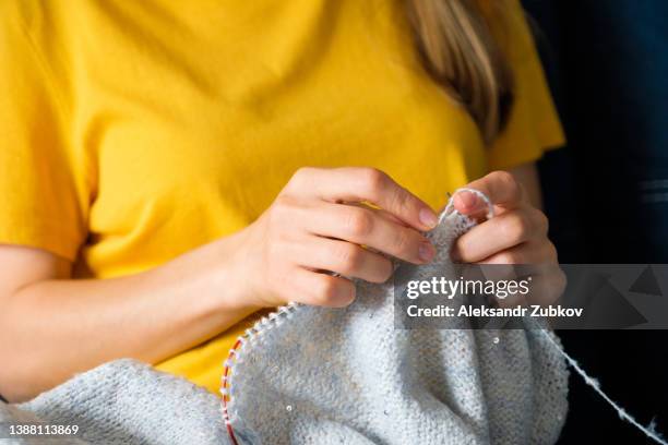 the girl is holding a knitting project and metal knitting needles in close-up. a woman knits a blue wool sweater or scarf, sitting on the couch at home. the concept of hobbies, creativity, needlework and manual work. creating clothes with your own hands. - ball of wool stock pictures, royalty-free photos & images