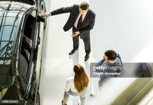 vista de arriba del vendedor feliz hablando con una pareja joven en la sala de exposición de automóviles. - salón de coches fotografías e imágenes de stock