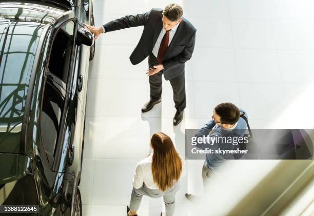 above view of happy salesman talking to young couple in car showroom. - bilförsäljare bildbanksfoton och bilder