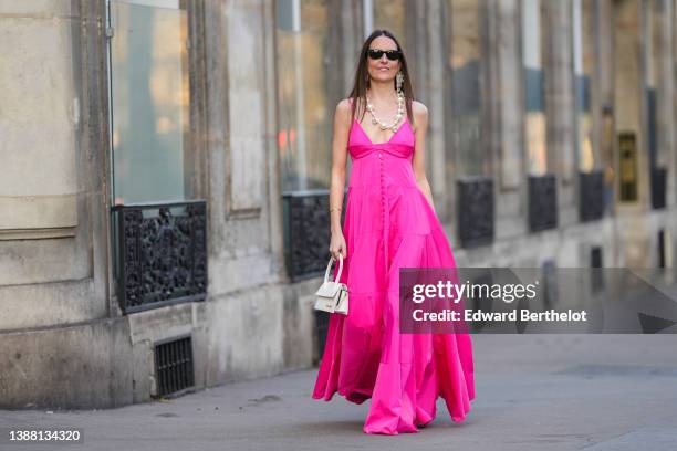 Alba Garavito Torre wears black sunglasses from Ray Ban, gold fringed metallic pendant earrings, a white oversized pearls long necklace, gold...