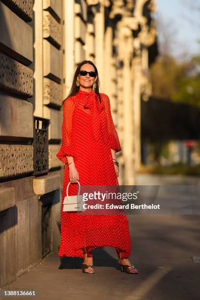Alba Garavito Torre wears black sunglasses from Ray Ban, gold fringed metallic pendant earrings, a red with beige polka dots print pattern knot high...