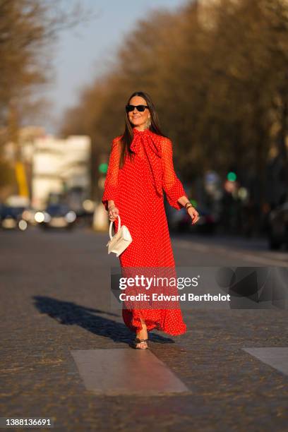 Alba Garavito Torre wears black sunglasses from Ray Ban, gold fringed metallic pendant earrings, a red with beige polka dots print pattern knot high...