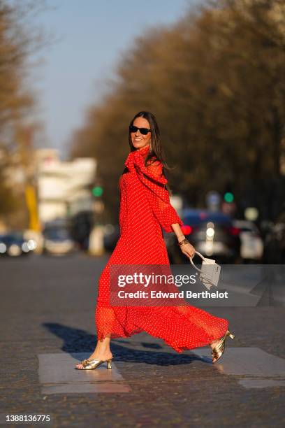 Alba Garavito Torre wears black sunglasses from Ray Ban, gold fringed metallic pendant earrings, a red with beige polka dots print pattern knot high...