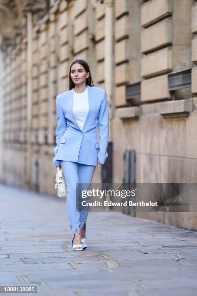 Diane Batoukina wears a white t-shirt, a pale blue blazer jacket from The Attico, matching pale blue slit / split suit pants from The Attico, a white...