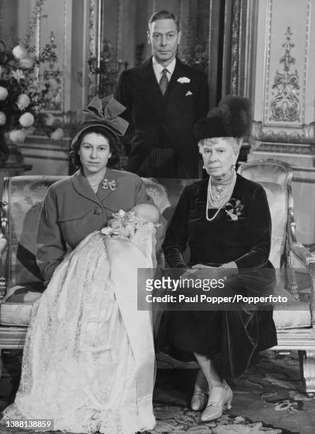 King George VI stands behind his daughter Princess Elizabeth, seated in centre, as she holds the infant Prince Charles, with great-grandmother Queen...