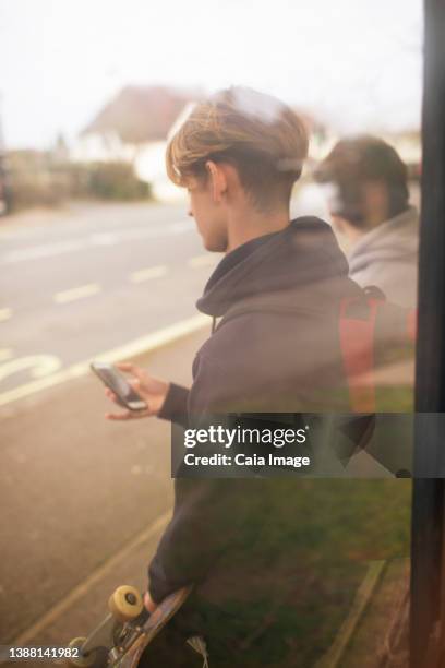 teenage boy with smart phone and skateboard waiting at bus stop - bus lane stockfoto's en -beelden